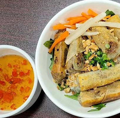 Vermicelli bowl with crispy spring rolls, peanuts and pickled vegetables beside a dipping sauce
