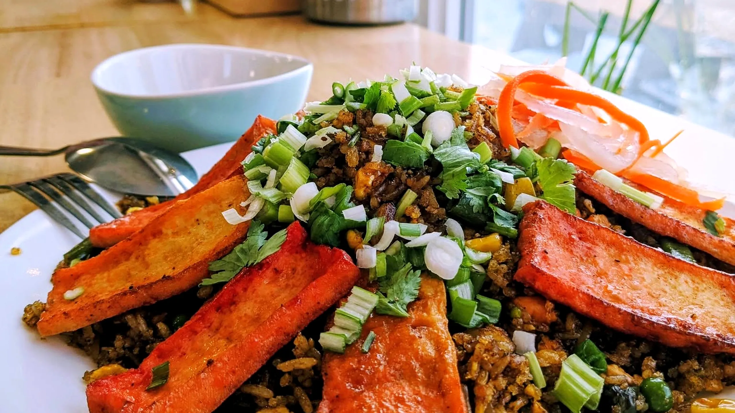 Fried rice topped with seared tofu slices, scallions and pickled carrot